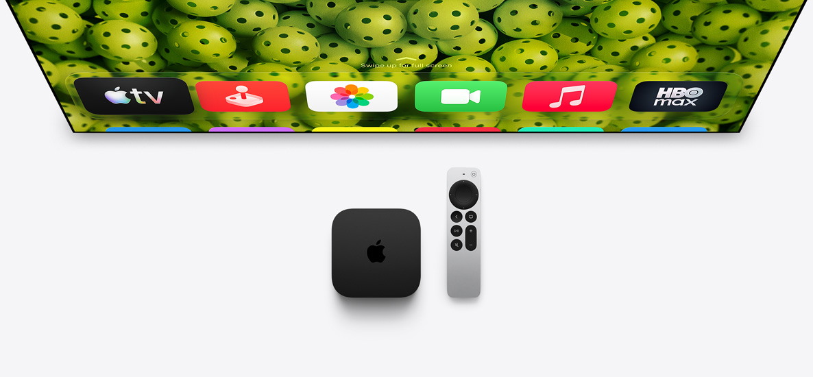 Apple TV 4K a Apple TV Remote pod televizní obrazovkou, na obrazovce je vidět horní řádek aplikací, na ploše je nastavená tapeta se zelenými míčky na pickleball