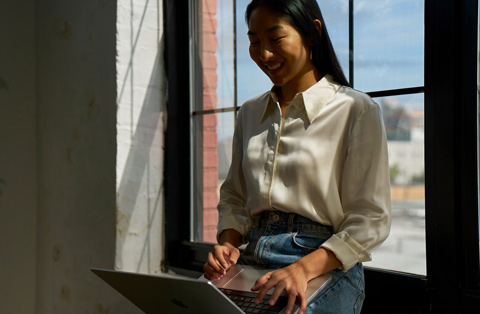 A person sitting on a windowsill smiles at the MacBook screen.