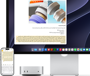 الجهة الأمامية لجهاز Mac mini، موضوع تحت شاشة Studio Display، جهاز iPhone موضوع على يمين الجهاز والشاشة، نص محدد مع أوامر القص والنسخ واللصق والتعبئة التلقائية في الجهة العلوية من iPhone يتطابق مع النص المظلل على الشاشة، في استعراض للحافظة العامة