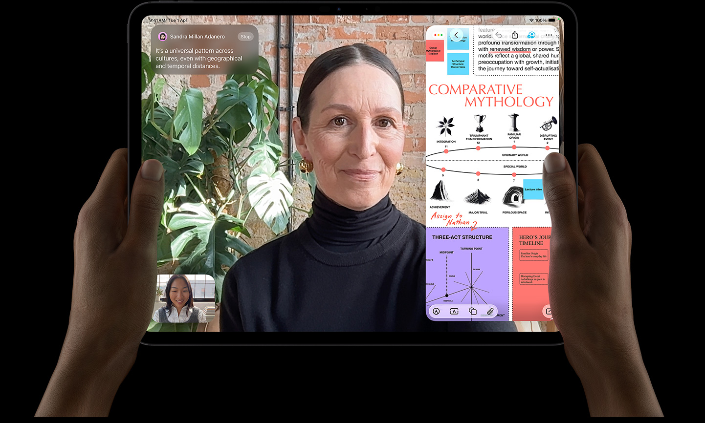 iPad Pro, front exterior, space black colour, left and right hands holding in landscape orientation, rounded corners, black display bezel, display showing a FaceTime conversation being live translated, and an educational app showing a presentation of 'Comparative Mythology' with text, diagrams, and handwritten notes