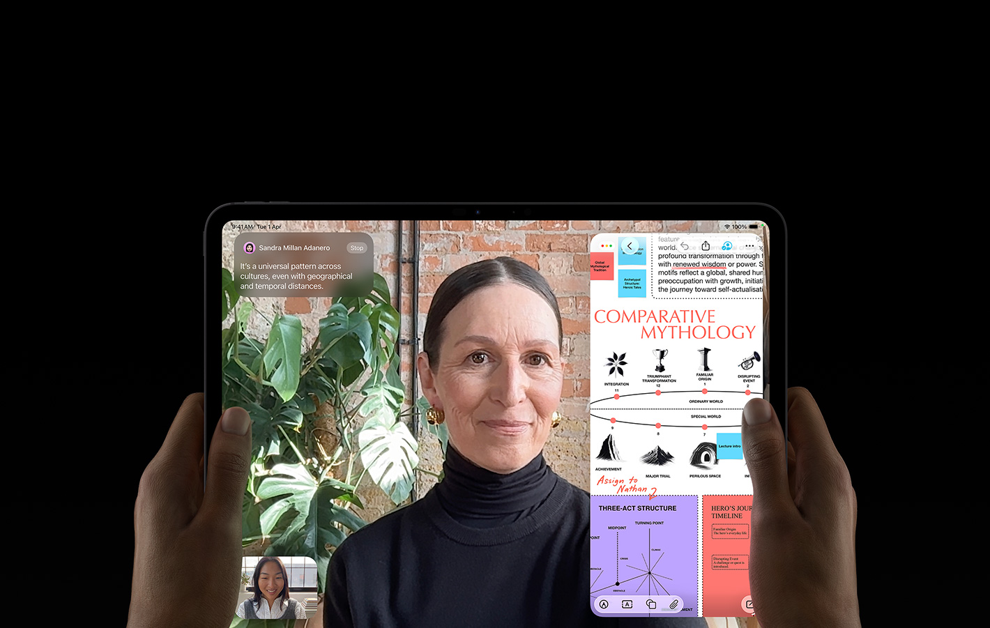 iPad Pro, front exterior, space black colour, left and right hands holding in landscape orientation, rounded corners, black display bezel, display showing a FaceTime conversation being live translated, and an educational app showing a presentation of 'Comparative Mythology' with text, diagrams and handwritten notes