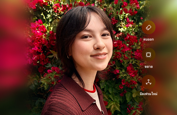 รูปภาพบุคคลที่มีผมสีน้ำตาลกำลังยิ้มแย้ม, สวมเสื้อสเวตเตอร์สีน้ำตาล, ล้อมรอบด้วยดอกไม้สีแดง, การสาธิตการปรับแต่งภาพถ่ายด้วย AI พร้อมตัวเลือกในการลบออก ขยาย และจัดเฟรมใหม่ที่แสดงอยู่เหนือภาพ