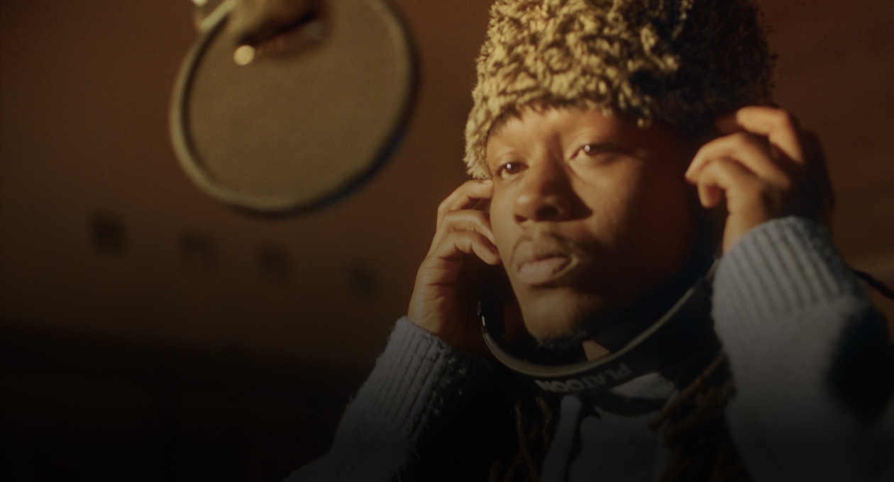 Photo of Kiddo K in music studio standing in front of recording mic and listening through headphones