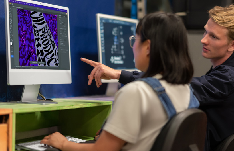 Deux personnes sont assises devant des moniteurs d’iMac affichant des modèles colorés, et l’une d’elles pointe un écran.