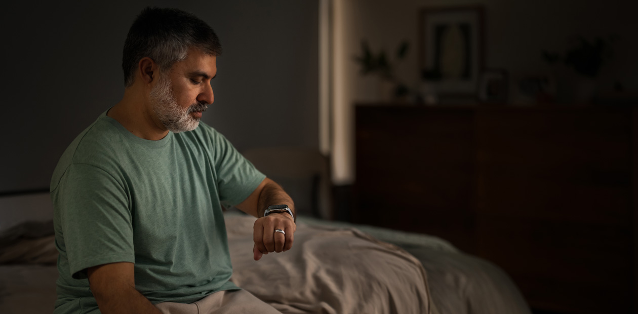 Homem sentado na cama verificando seu Apple Watch.