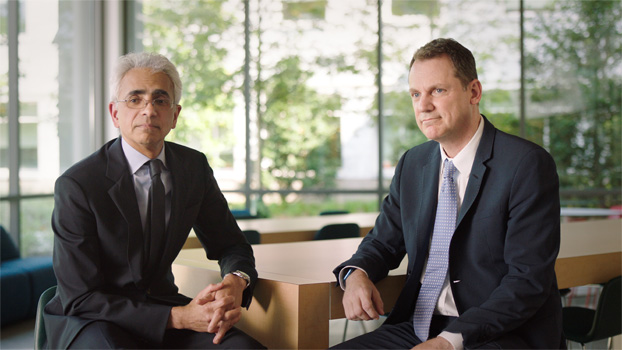 Dos personas con trajes sentadas a una mesa.