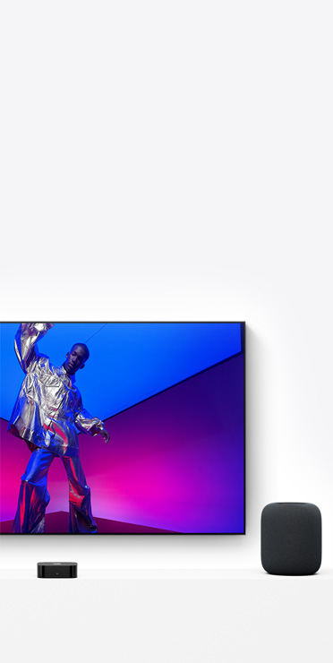 Apple TV 4K und HomePod, Farbe Mitternacht, der Fernseher zeigt eine Person in einem metallisch silbernen Outfit