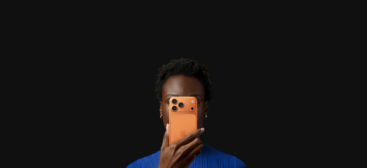 A person holds iPhone 17 Pro in front of their face, back exterior facing outward, Cosmic Orange color.