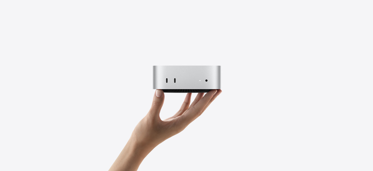 Μπροστινή όψη του Mac&nbsp;mini ισορροπημένου στα δάχτυλα ενός χεριού που τεντώνεται προς τα πάνω, η μπροστινή όψη δείχνει δύο θύρες Thunderbolt, ενδεικτική λυχνία κατάστασης και υποδοχή ακουστικών, κωνική μαύρη βάση στο κάτω μέρος, επίπεδο επάνω μέρος, στρογγυλεμένες πλευρές, ευθείες άκρες, ασημί χρώμα