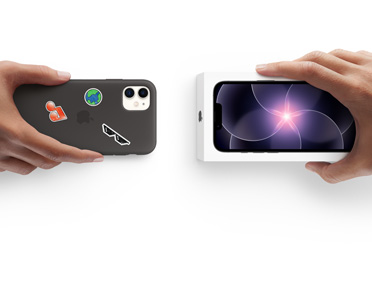 Due mani che si scambiano un iPhone 13 usato con custodia in silicone coperta di adesivi sul retro e un iPhone 17e nuovo ancora nella sua confezione