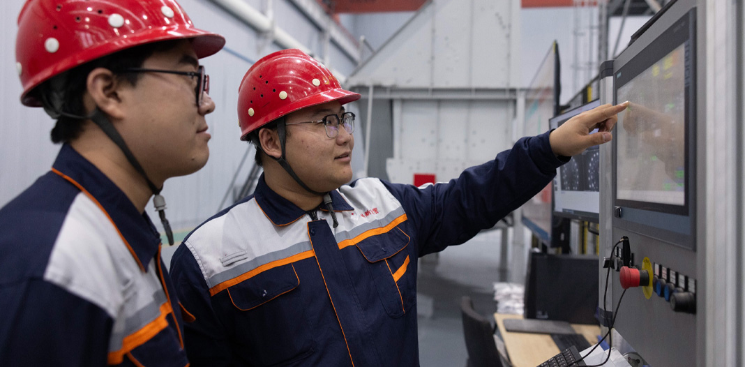 Deux employés portant un casque de sécurité et un uniforme regardent un écran numérique avec des commande en bas