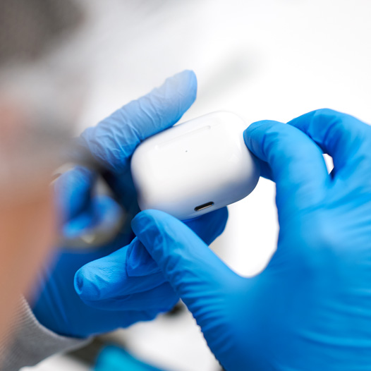 Deux mains munies de gants en latex tiennent un étui d’AirPods