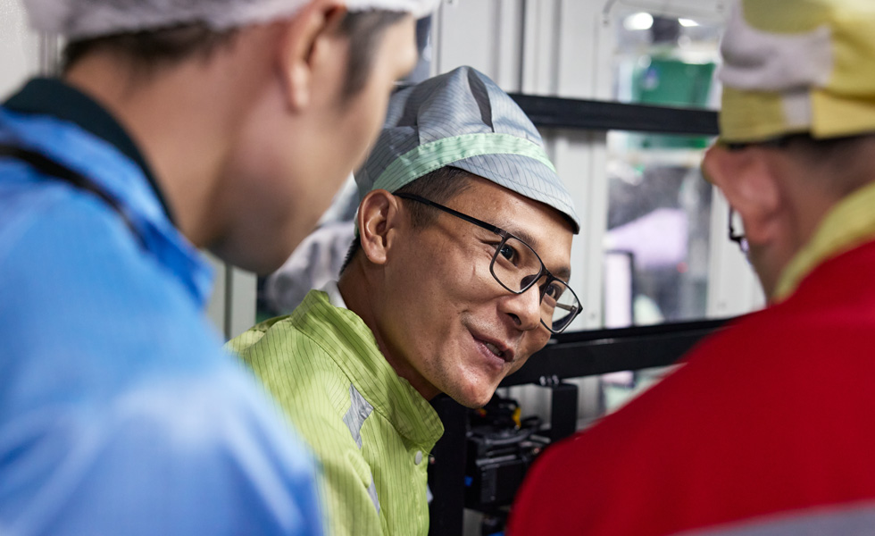 Trois personnes en uniforme de travail discutant près d’une machine d’assemblage d’AirPods Pro