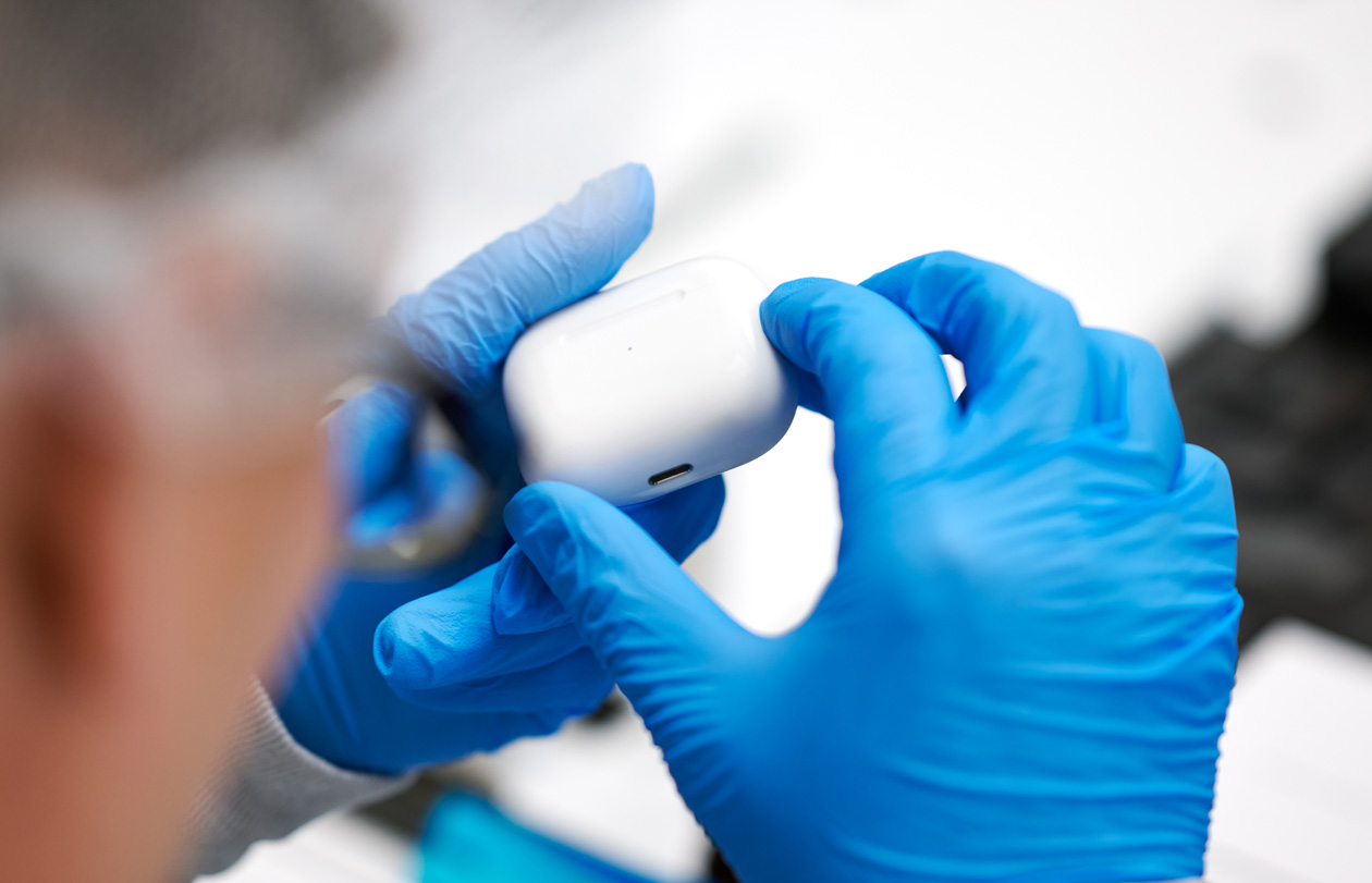 Deux mains munies de gants en latex tiennent un étui d’AirPods