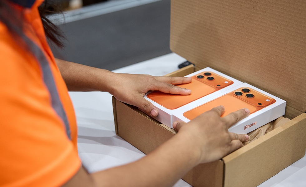 Worker placing boxed iPhone devices into a shipping carton.