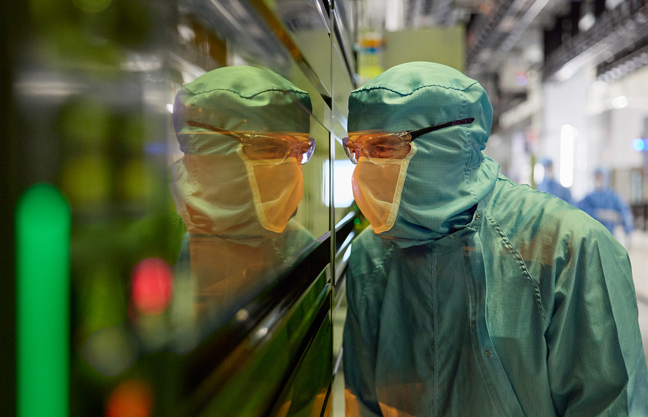 An employee in full-body work suit peers into a window of a manufacturing machine