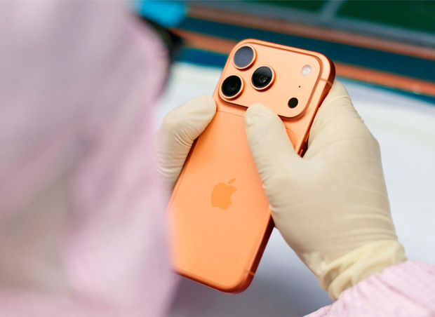 An employee in full-coverage work suit inspects an iPhone at a work station